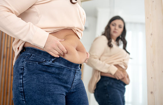 Mulher observando o próprio corpo em frente ao espelho, simbolizando a preocupação com ganho de peso e os efeitos do Implanon na saúde e na fertilidade.